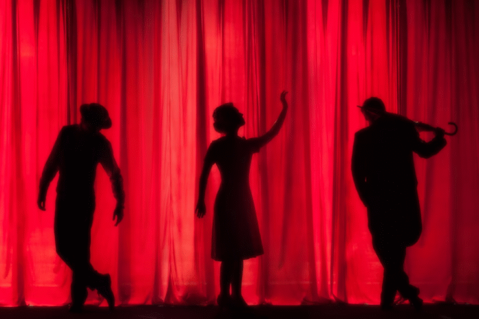 Red theatre curtain with three performers on stage