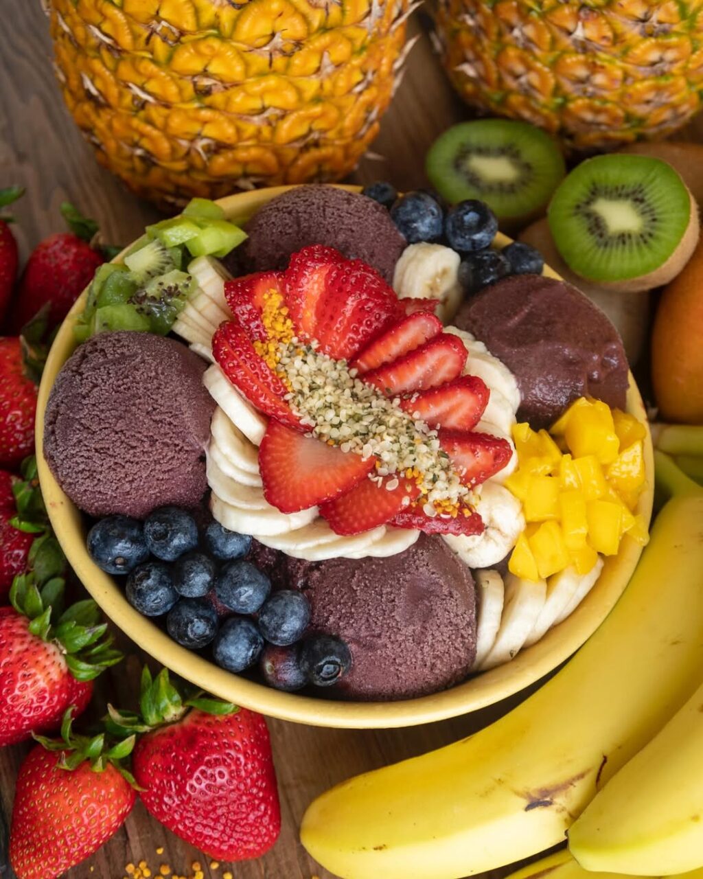 Ubatuba Açaí bowl topped with strawberries, blueberries, banana, mango, and kiwi surrounded by fresh fruit.