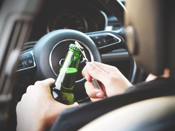 Person opening an alcohol bottle inside a car, illustrating the risk of drunk driving. Photo by energepic.com.