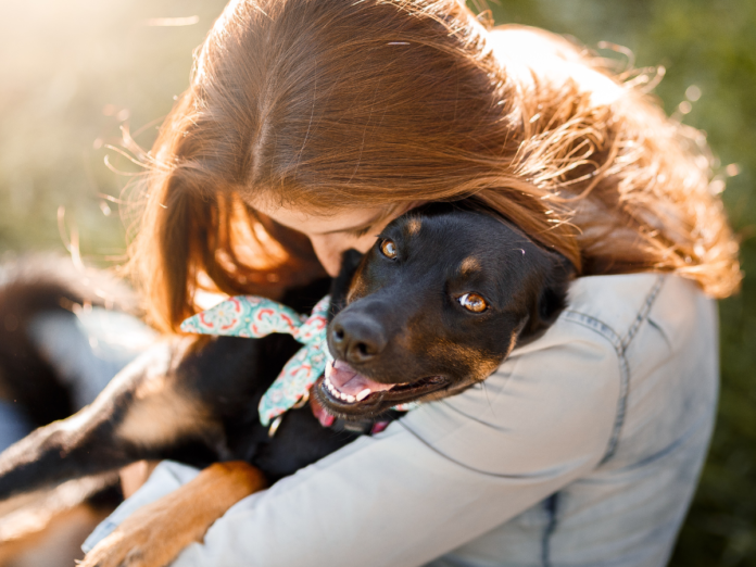 Person hugging a happy black dog outdoors during a pet adoption moment.