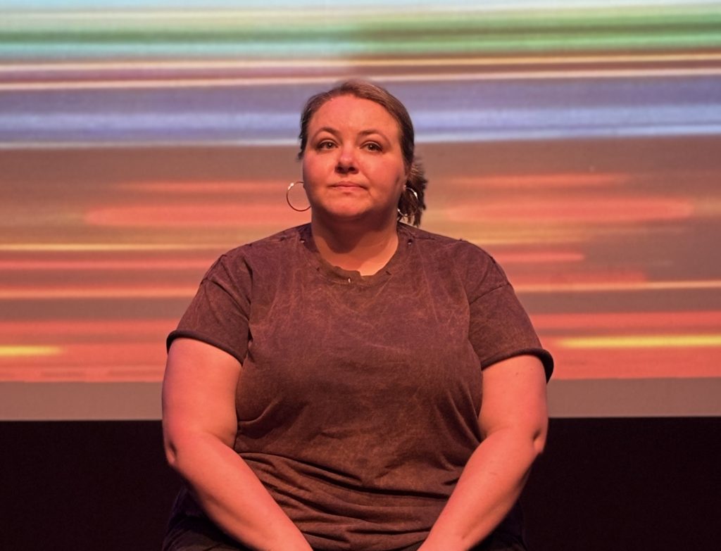 Marissa Fennell seated onstage in It’s All a Joke at Solofest 2026