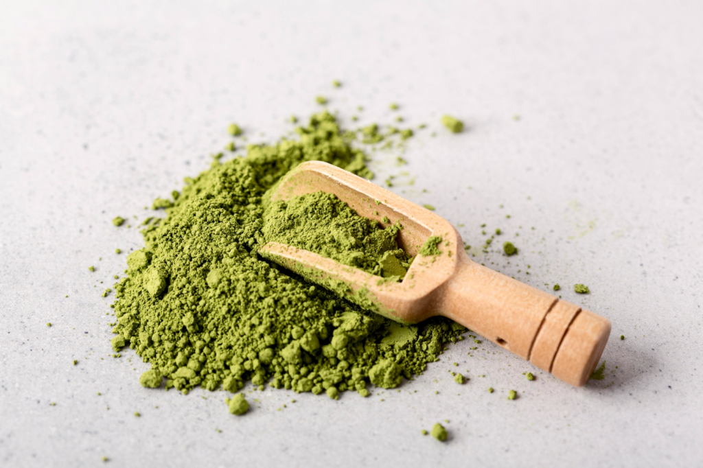 Green kratom powder with wooden scoop on a light surface
