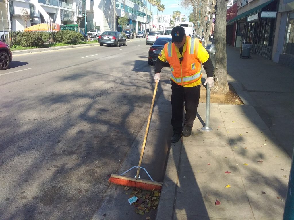NoHo BID maintenance worker sweeping leaves and debris from a North Hollywood sidewalk.