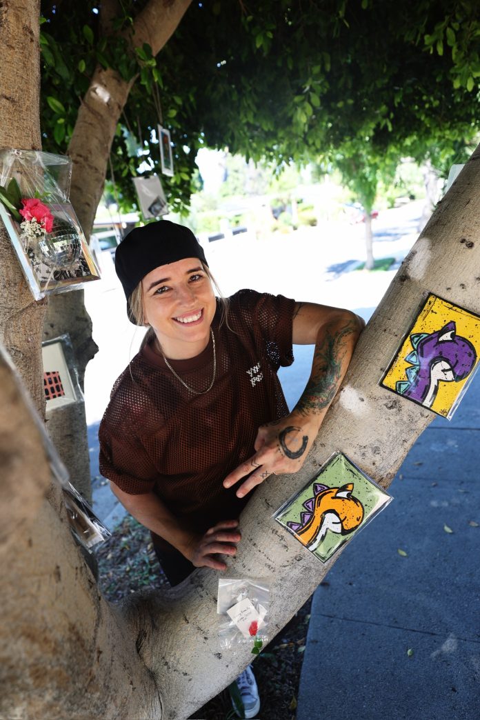 Stacey Hughes displaying small 8-bit resin tile artworks attached to a tree outdoors in North Hollywood