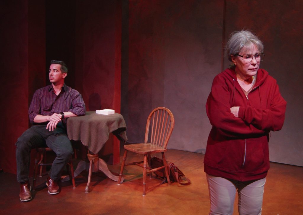 Taylor Gilbert as Lois stands in the foreground while Danny Lee Gomez as Tim sits behind her at a table in Hell Mouth at The Road Theatre in NoHo Arts District