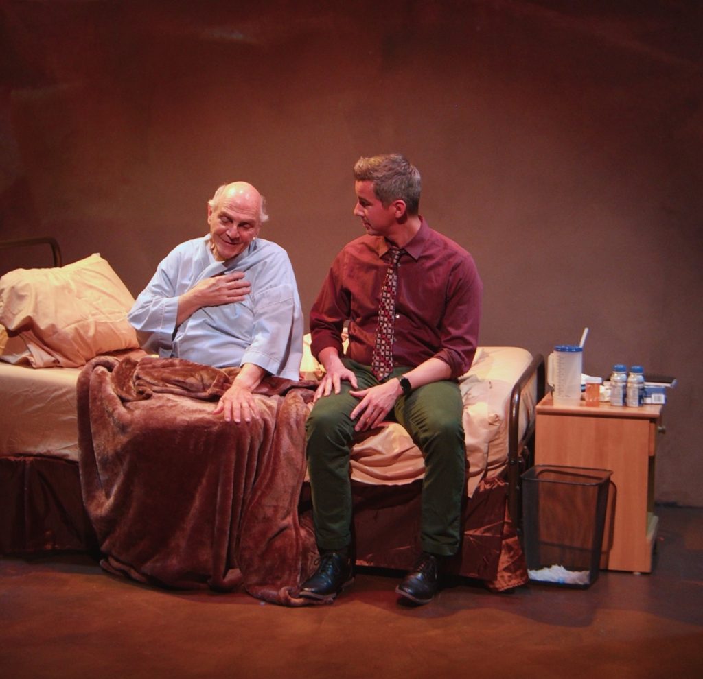 Tony Abatemarco as Russell sits in a hospital bed speaking with Danny Lee Gomez as Tim in Hell Mouth at The Road Theatre in NoHo Arts District