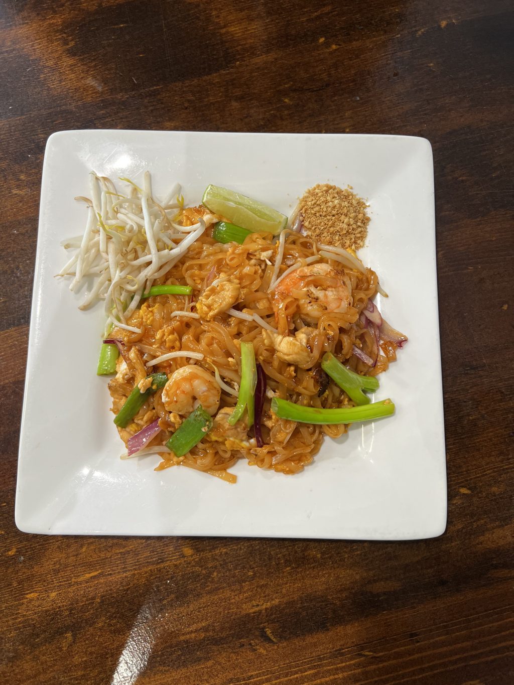 Pad Thai with shrimp, bean sprouts, and lime on white plate at Delish Thai Kitchen