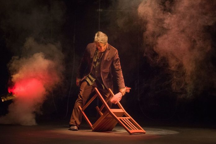 Shahin Sayadi in Ritual Music to Cure a Lover performing with chair on stage surrounded by theatrical smoke and lighting