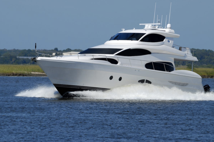 White motor yacht cruising at speed on open water with shoreline in the background