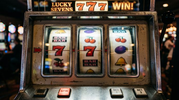 Close-up of a slot machine with spinning reels showing sevens and fruit symbols in a casino setting