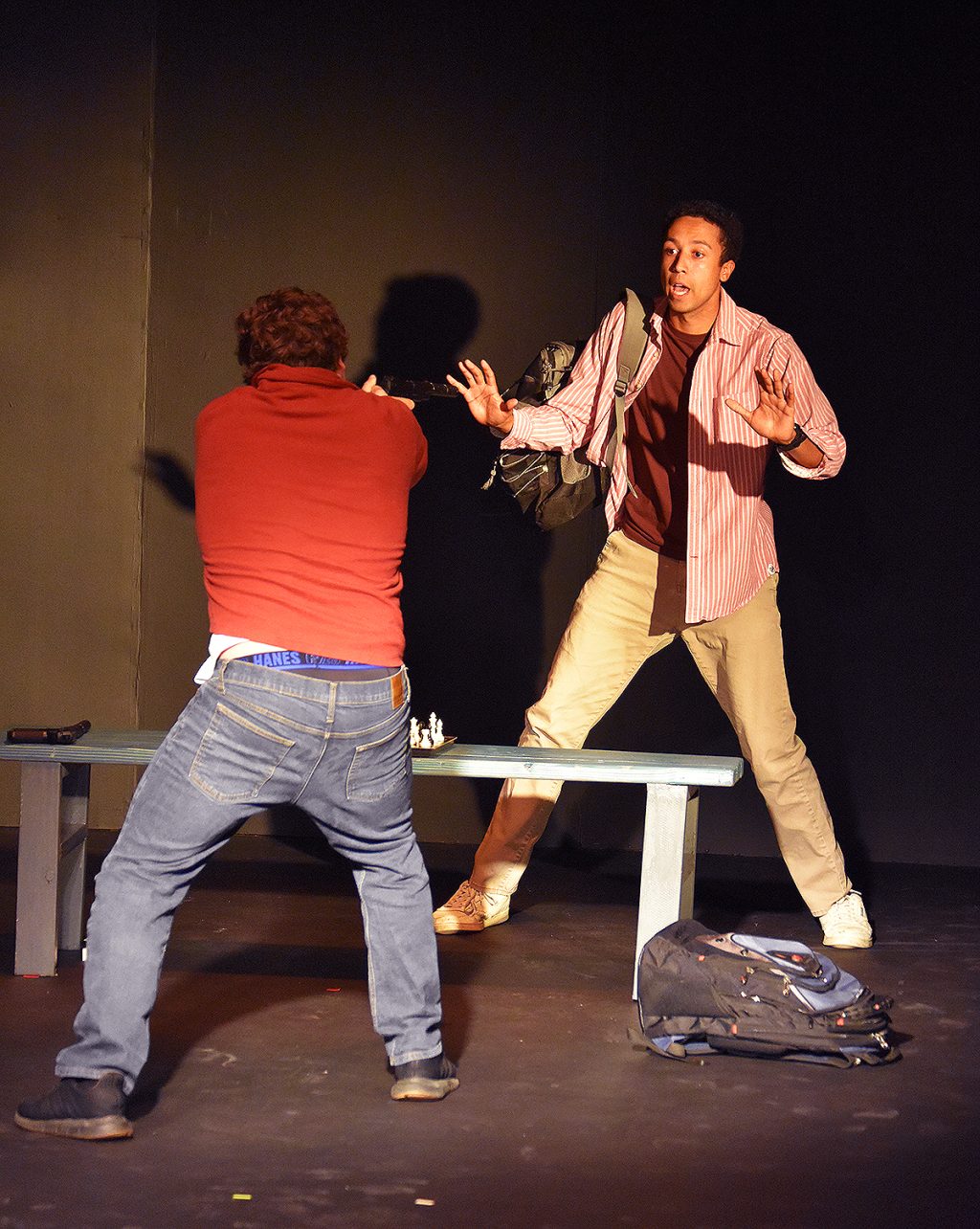 Twisted theatre review moment showing gun confrontation between two men across a bench on stage at Theatre West