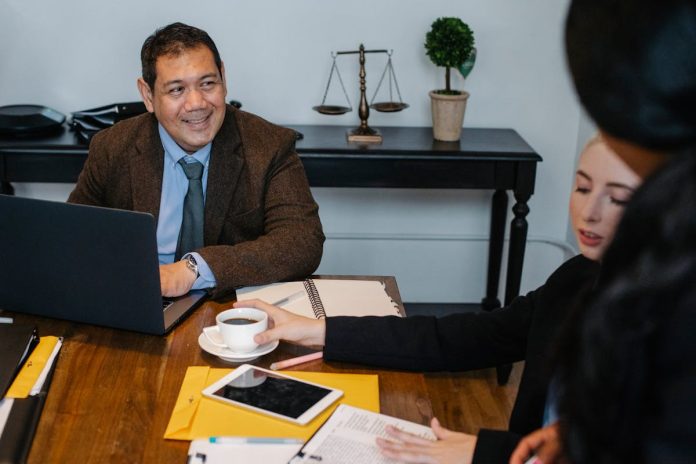Attorney meeting with two clients at a desk, discussing a wrongful death claim with legal documents and laptop visible in an office setting
