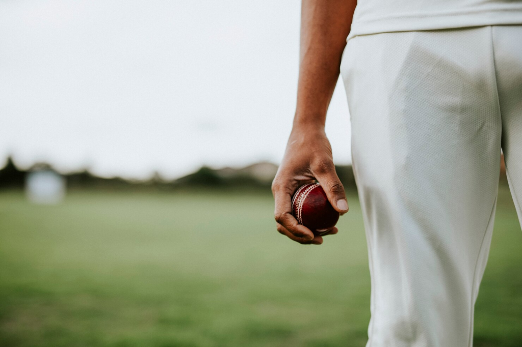 Close-up of a cricketer holding a red ball on the field during a match