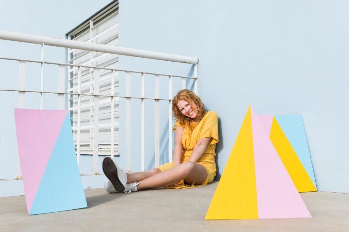 woman in yellow outfit sitting on floor with colorful geometric panels, bold personal style in creative setting