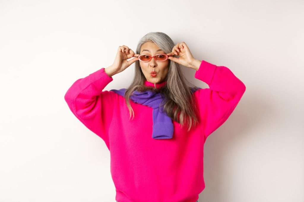 woman in bright pink sweater adjusting sunglasses, expressive personal style and bold fashion look