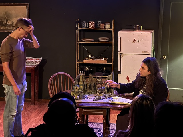 Actors perform a dramatic tabletop scene with miniature set pieces in An Ode to Parenting play