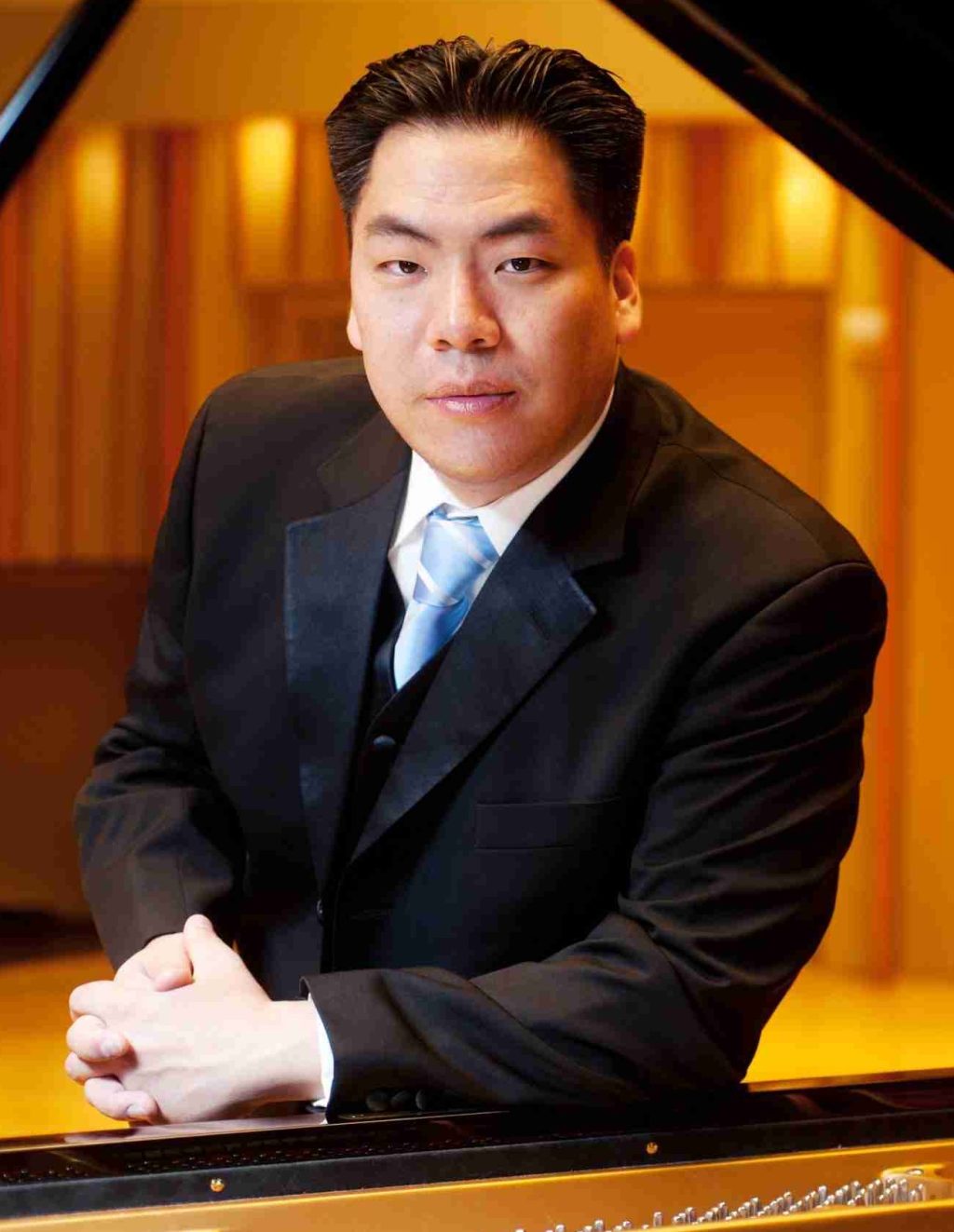 Rufus Choi seated at a piano in formal attire in a concert hall setting