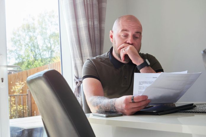homeowner sitting at table reviewing foreclosure notice and bills, calculator and paperwork visible, natural light, realistic photography, no text, emotional but not dramatic