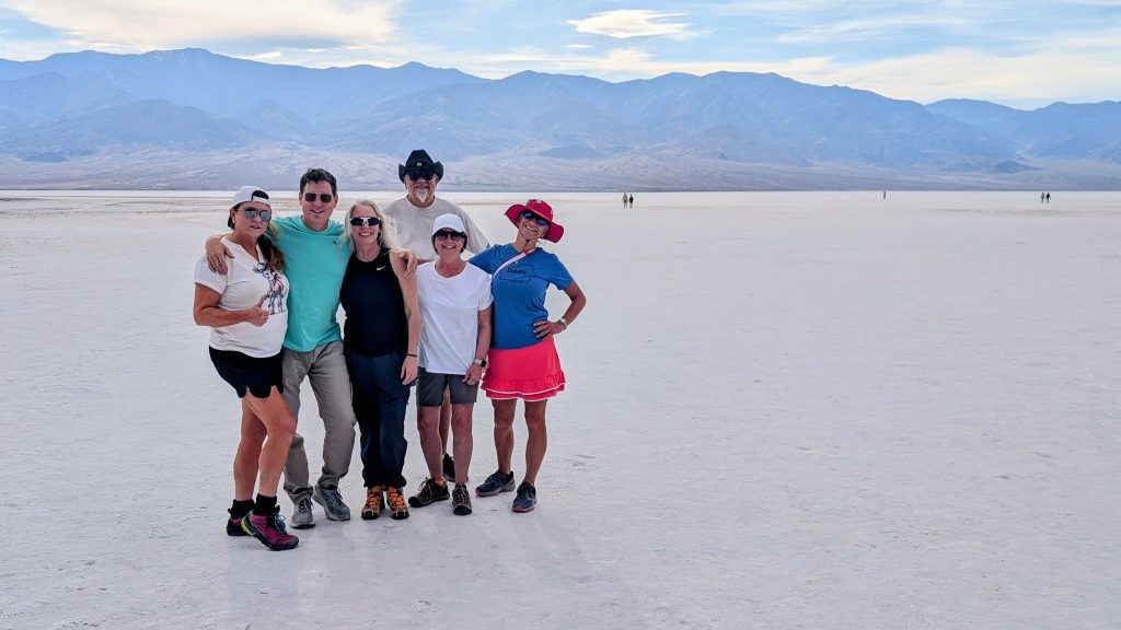 Travelers standing on the salt flats of Badwater Basin in Death Valley National Park with mountain views in the background.
