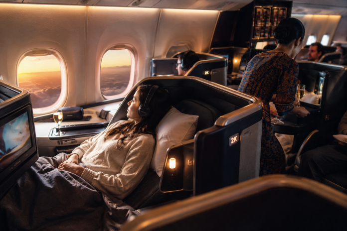 ChatGPT Image May 19, 2026, 08_11_07 PM Passengers relaxing in a modern business class airplane cabin with lie-flat seats, champagne service, ambient lighting, and sunset views during an international flight.
