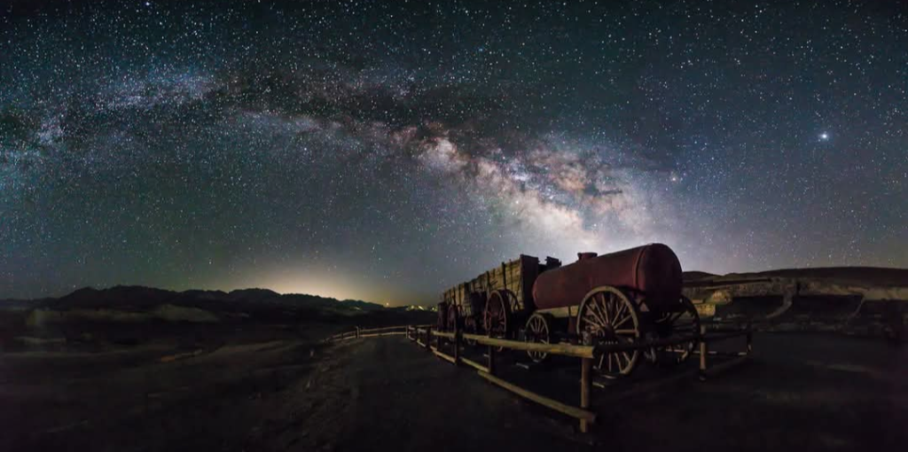 Milky Way stretching across the night sky over historic wagons in Death Valley National Park during a dark sky stargazing experience.