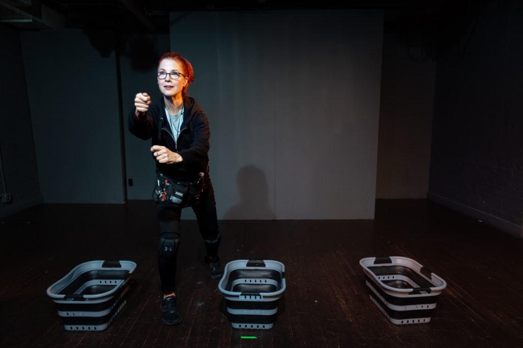 Kimberly Prentice performs in UNSEEN at the 2026 Hollywood Fringe Festival, portraying a backstage Broadway dresser surrounded by costume bins onstage.
