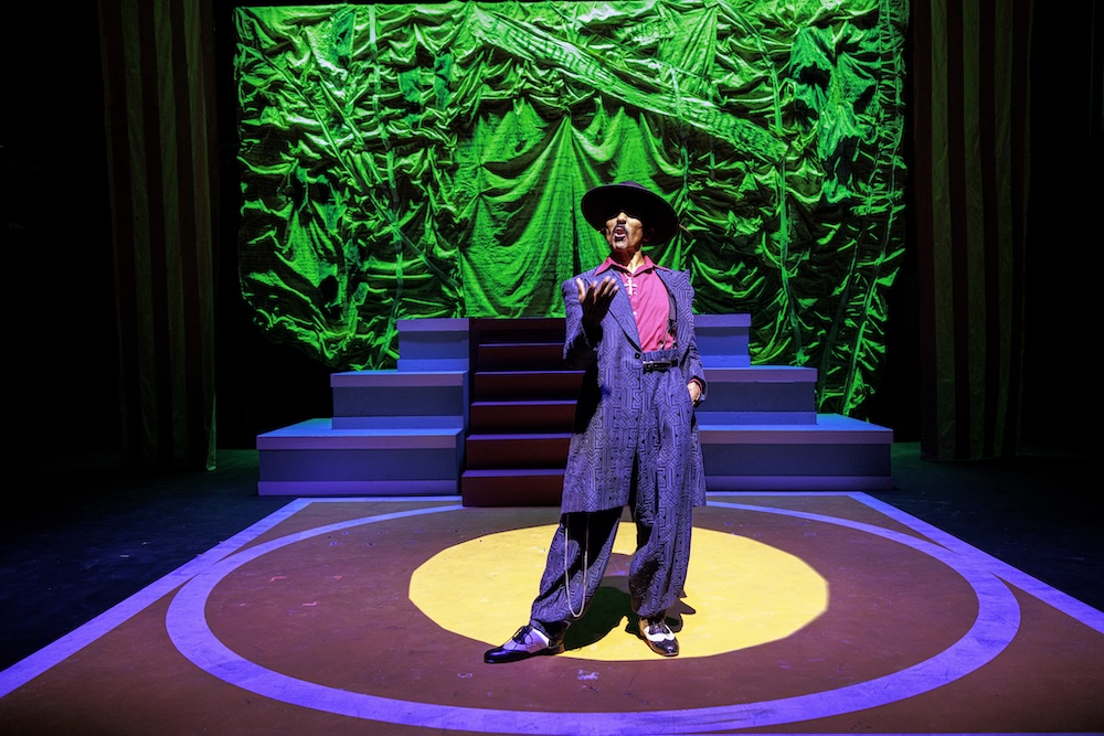 Raúl Cardona as El Pachuco performs under dramatic green stage lighting in Los Angeles Mission College’s production of Zoot Suit by Luis Valdez.