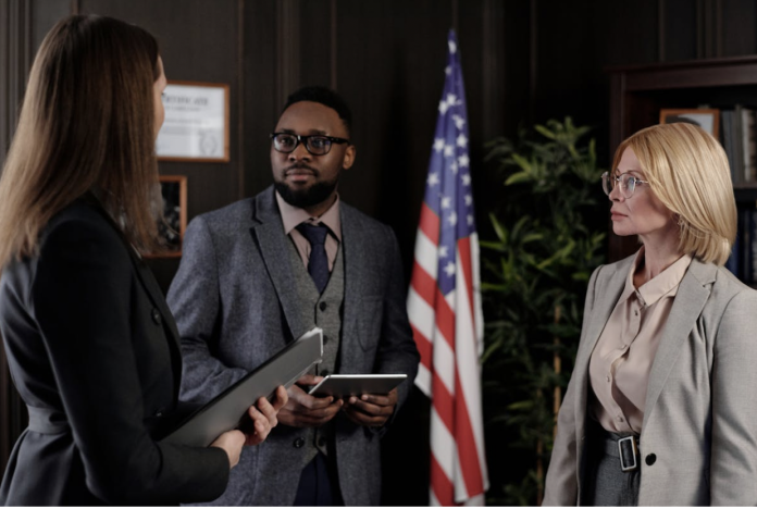 Screen Shot 2026-05-25 at 3.55.48 PM Lawyers and legal professionals discussing a California personal injury case inside a modern office with legal documents, tablets, and an American flag in the background.