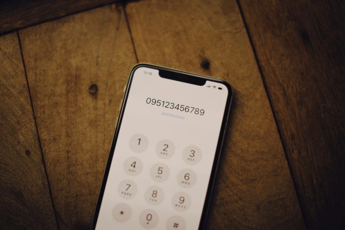 alexey-demidov-kbpn6F0-Ygs-unsplash Smartphone displaying a virtual phone number on a dialing screen placed on a wooden table, representing freelance business communication and virtual phone services.