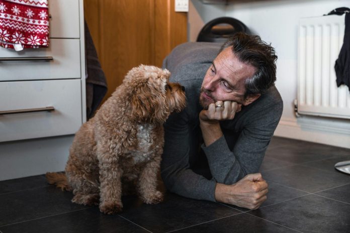 Pet owner lying on the kitchen floor beside an injured or recovering dog, providing comfort and companionship during home recovery and rehabilitation.