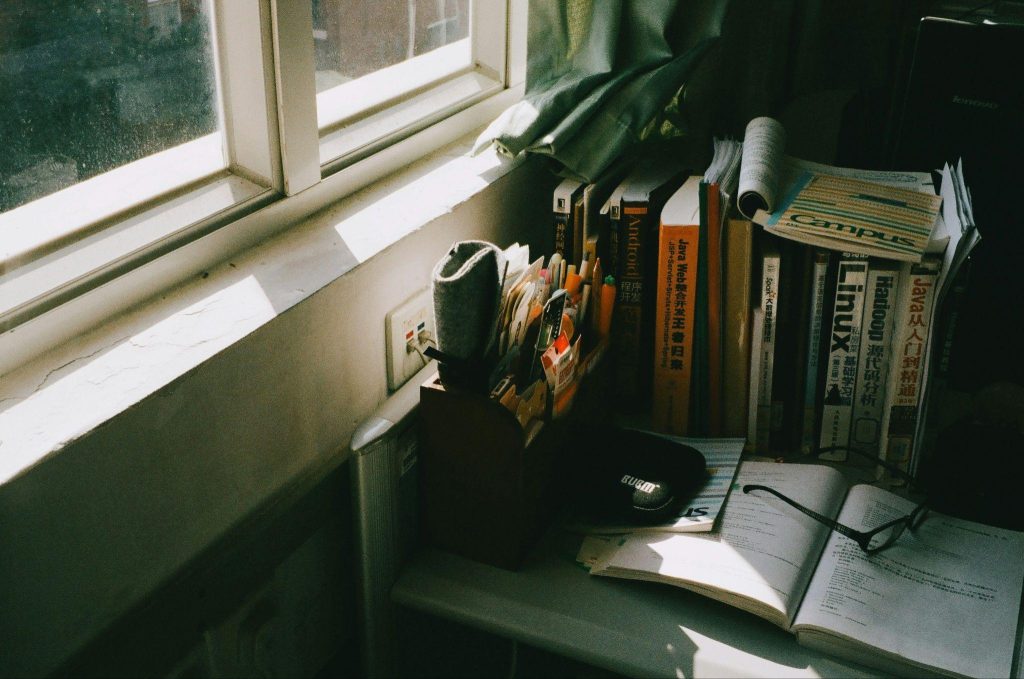Softly lit cluttered desk with books, papers, and window light showing visual noise in a home environment