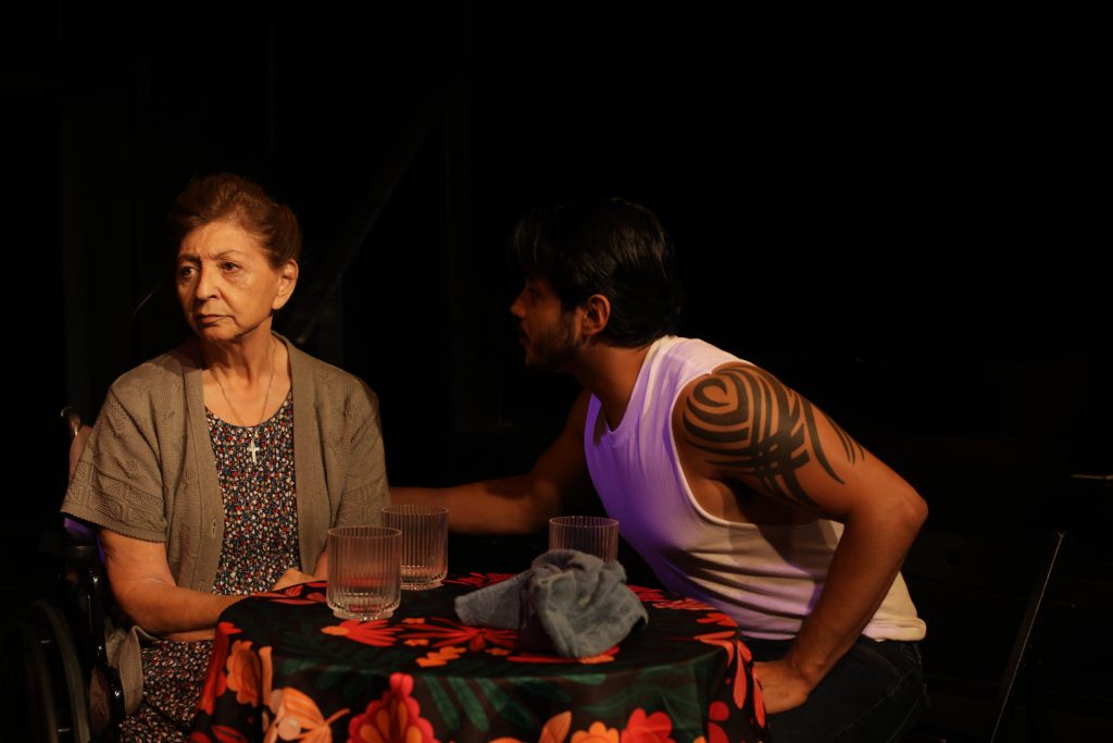 A family conversation unfolds in Punish Me as an elderly woman sits at a table with a younger man.