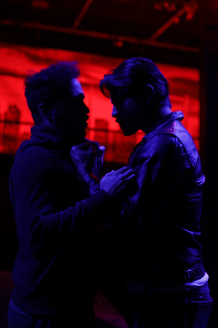 AVIK7147 Two lead characters share a dramatic moment under red and blue stage lighting in Punish Me.