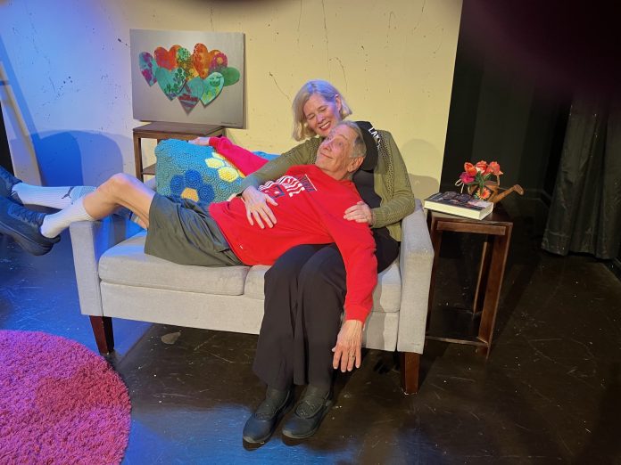 Act Your Age! photio 2 Act Your Age cast members share a tender moment on a living room set at Two Roads Theatre.