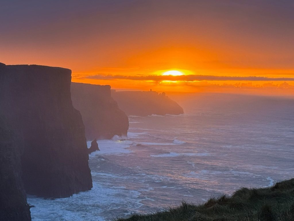 Sunset over the Cliffs of Moher as waves crash against Ireland's dramatic Atlantic coastline.