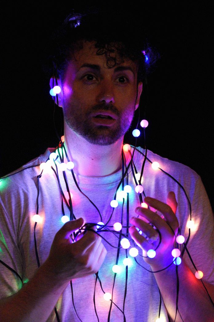 Danilo Napoli wrapped in colorful string lights during his solo performance of The Show Has Been Cancelled (Due To the End of the World) at the 2026 Hollywood Fringe Festival.