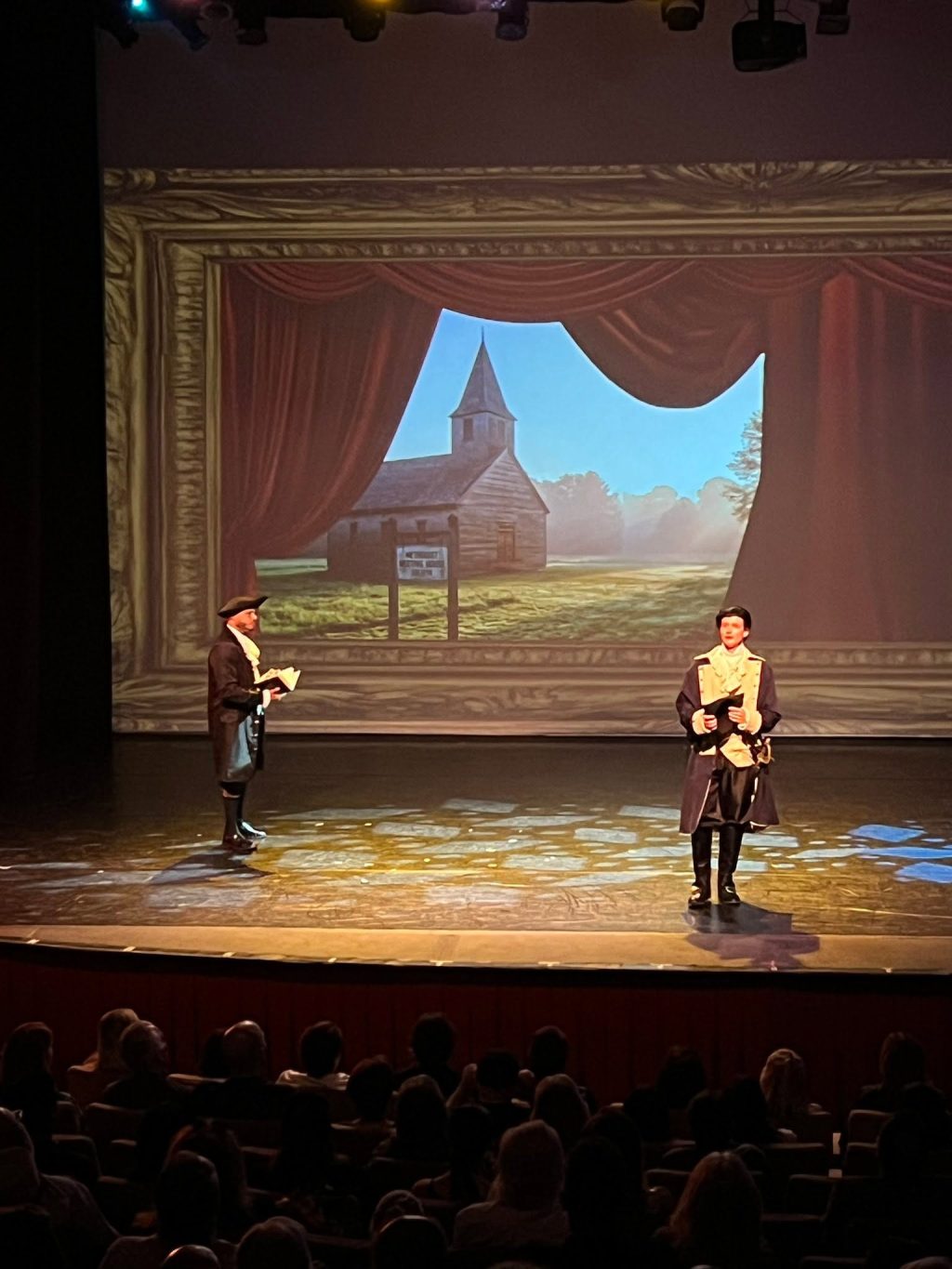 A scene from The Fighting Quaker at El Portal Theatre features actors in 18th-century costume against a colonial church backdrop, highlighting the play's celebration of America's 250th anniversary and the life of Timothy Matlack.
