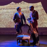 Period-costumed actors perform in The Fighting Quaker at El Portal Theatre, standing before a projection of the Declaration of Independence as Timothy Matlack's role in American history comes to life.