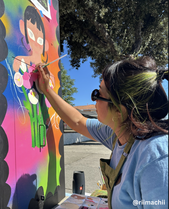 Artist @riimachii paints a colorful floral design on a utility box as part of the Streetbox Art Project.