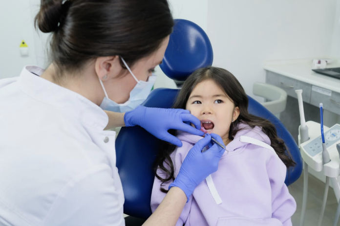 Pediatric dentist examining a young child's teeth during a dental visit to evaluate tooth decay and determine if a dental crown is needed.