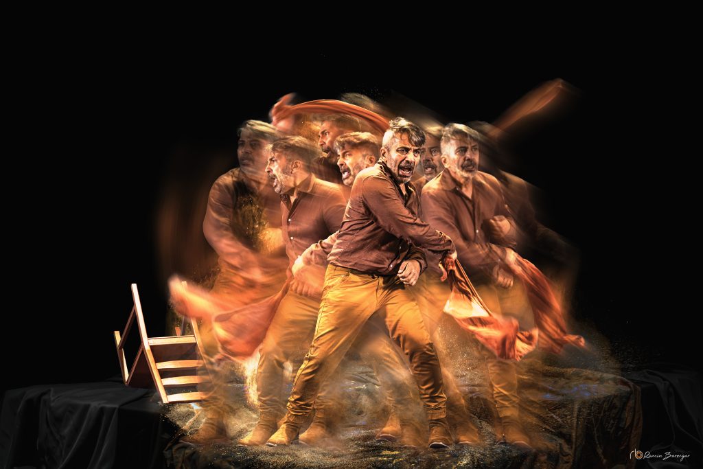 Shahin Sayadi in Ritual Music to Cure a Lover performing with chair on stage surrounded by theatrical smoke and lighting fire