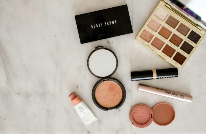 image Makeup and beauty products arranged on a marble surface, including blush, lipstick, eyeshadow palette, and cosmetics used in an at-home beauty routine.