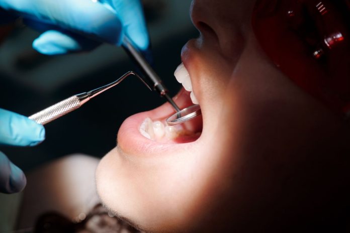 Dentist examining a patient's teeth with a dental mirror and scaler during a routine oral health check before or after dental implant treatment.