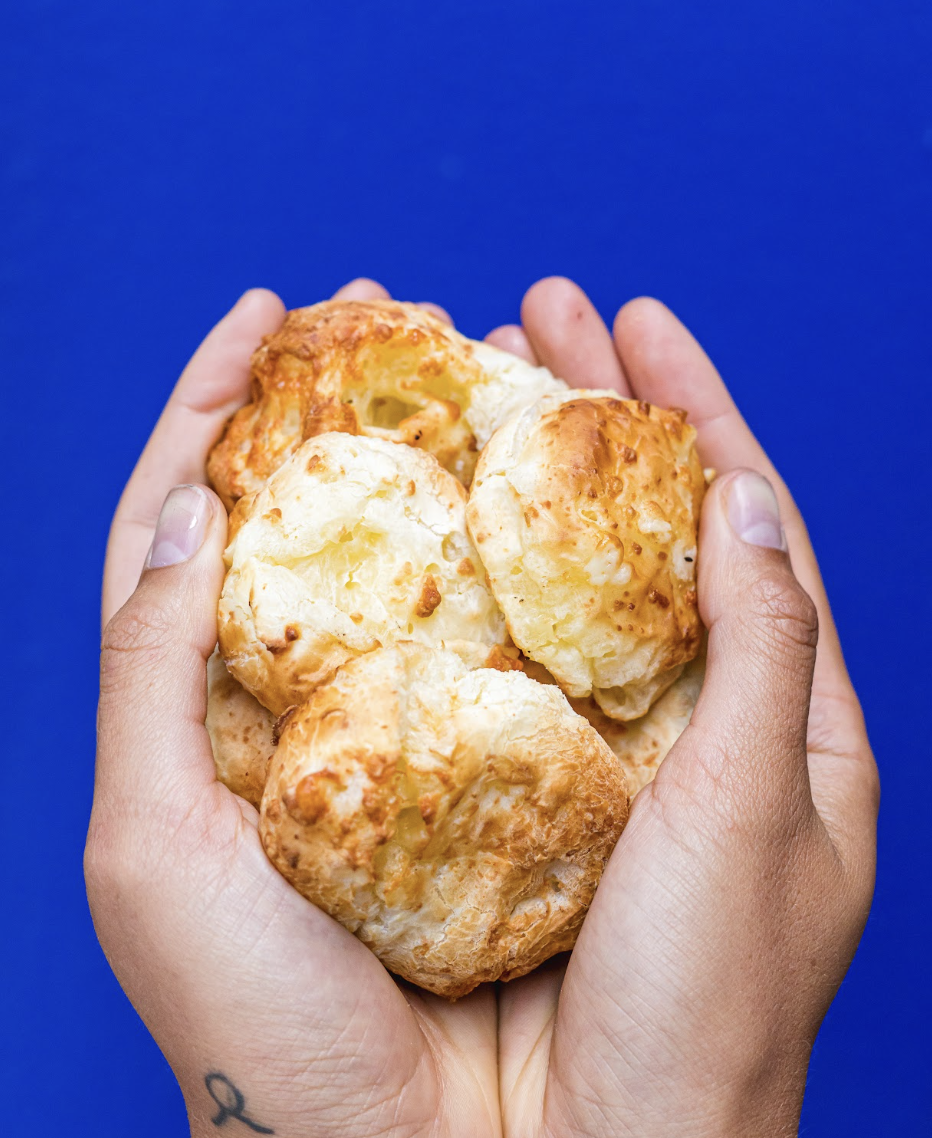 Hands holding freshly baked Brazilian pão de queijo cheese bread.