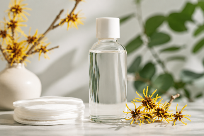ChatGPT Image Jul 1, 2026, 05_22_56 PM Bottle of alcohol-free witch hazel with cotton pads and witch hazel flowers, illustrating a natural skincare treatment for acne-prone skin.