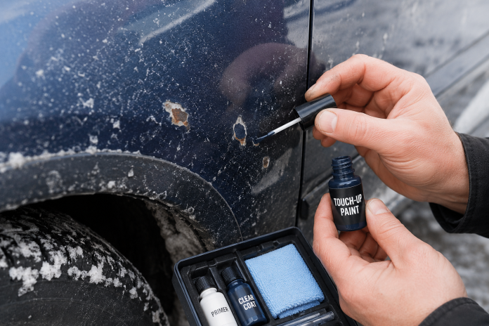 Close-up of chipped car paint with winter road salt as a person repairs the damaged paintwork using a touch-up paint kit.