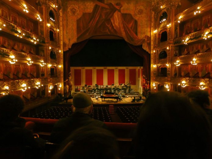 image Audience view of a grand theater featuring an illuminated stage, ornate balconies, and classic architectural details.