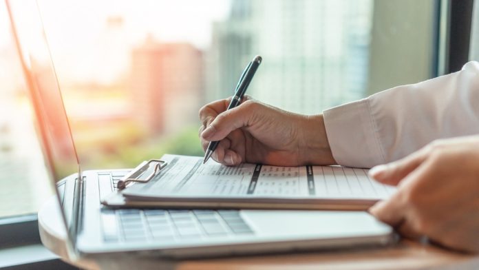 Attorney reviews and signs legal documents on a clipboard beside a laptop while preparing an injury claim after a car accident.