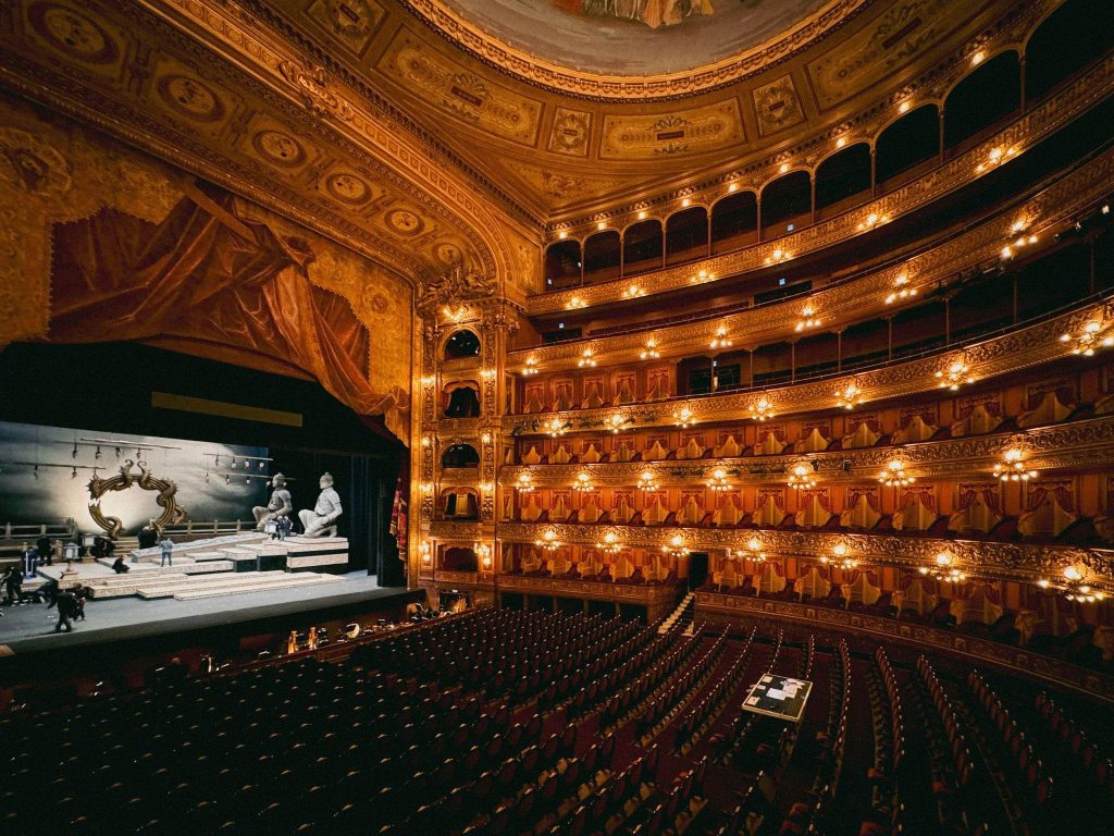 Elegant theater interior with ornate balconies, warm lighting, and a stage set for a performance.