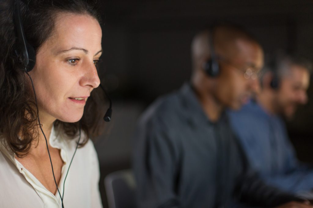 Outbound call center team wearing headsets and working at computers in a modern office.